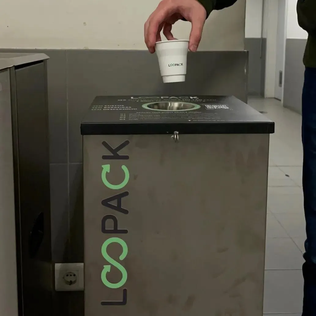 A hand dropping an RFID-tagged reusable cup into the opening of the Loopack smart return bin.