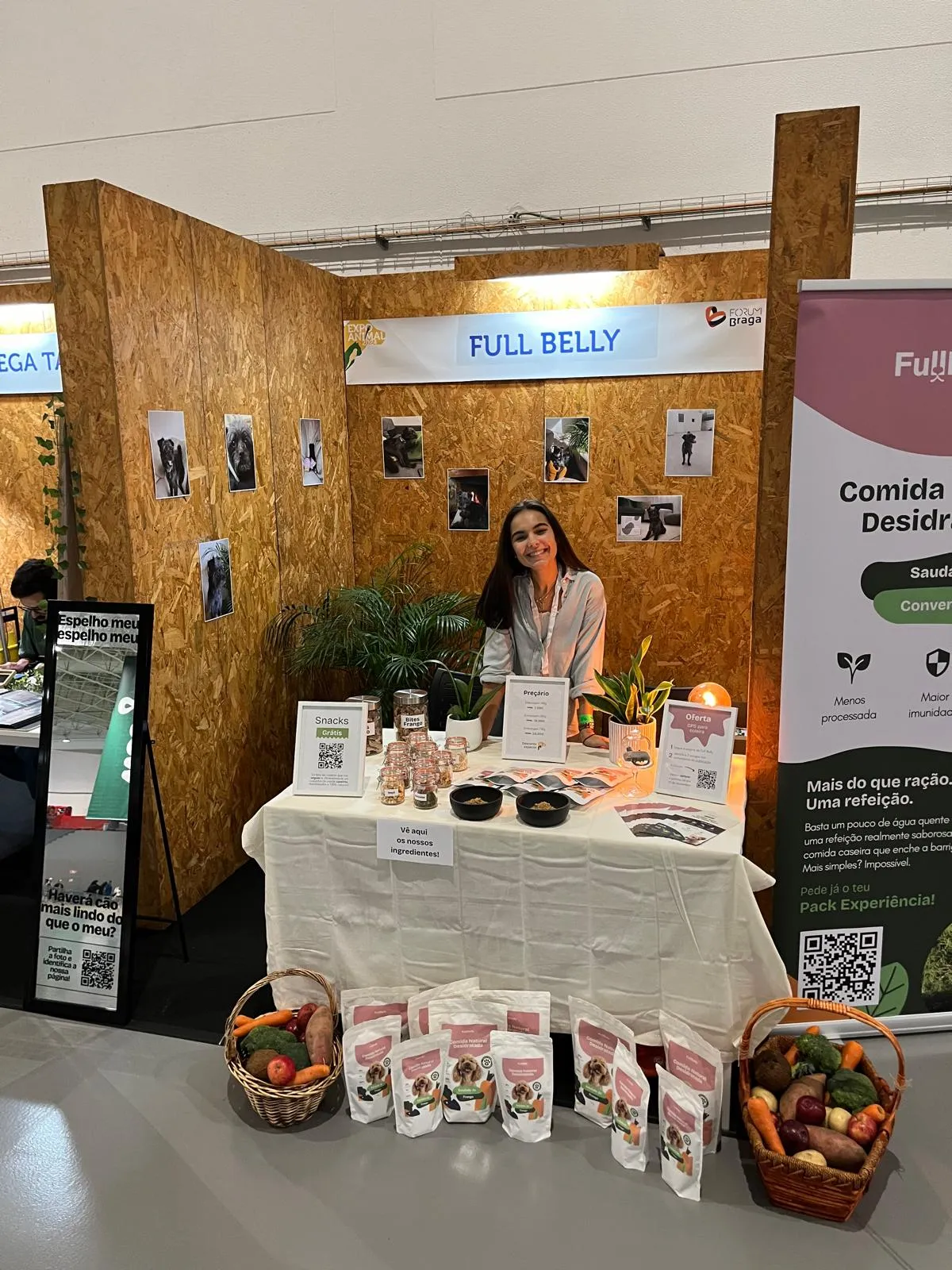 The Full Belly stand at a pet industry fair, with product pouches laid out on a table and baskets of vegetables in front of it.