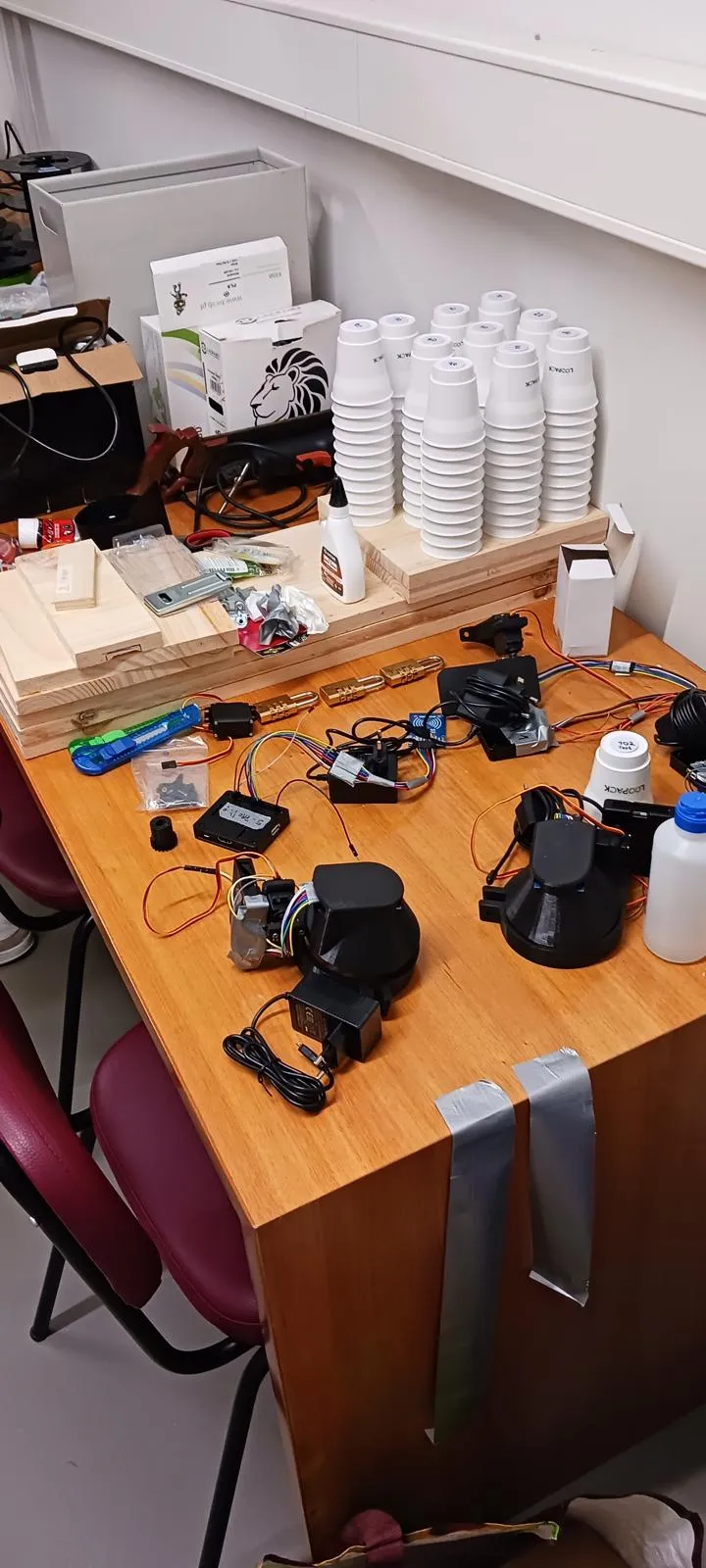 A workbench covered with early Loopack prototype materials: stacks of reusable cups, plywood parts, motors, wiring and electronics.